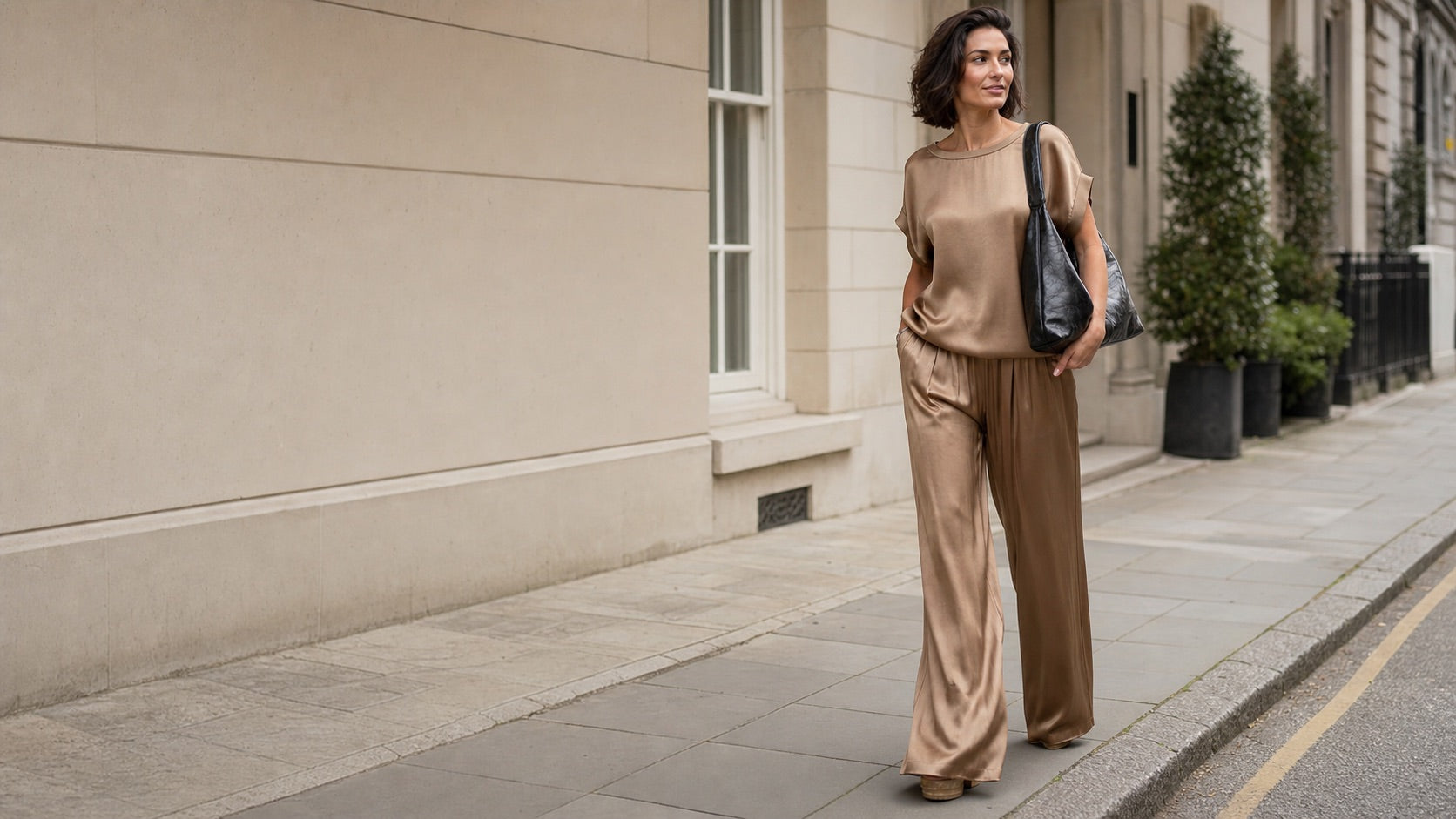 Woman wearing a Roseford satin trouser set and carrying a black shoulder bag on a London street